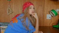 Danielle Marsh in a blue oversized shirt and red bandana, posing thoughtfully against a wooden backdrop.