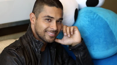 Smiling Actor with Facial Hair Posing Next to a Blue Plush Toy