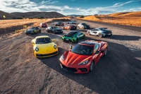 Una impresionante alineación de coches deportivos de alto rendimiento, incluyendo el BMW M2 Competition, Chevrolet Corvette Stingray, Porsche 911 Carrera S y más, contra un fondo escénico de colinas onduladas y cielos azules.