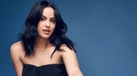 Camila Mendes in einem stilvollen Fotoshooting vor einem blauen Hintergrund.