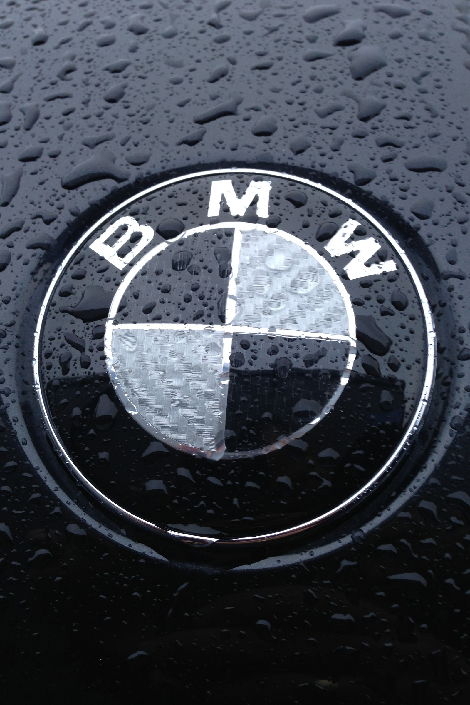 A close up of a bmw emblem on a wet black car (bmw, carbon, fibre, m sport, m3)