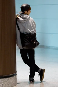 Xiumin from EXO in a casual outfit leaning against a pillar.