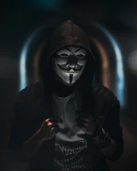 Eine Figur, die eine Guy-Fawkes-Maske und eine Kapuze trägt, steht in einem dunklen, beleuchteten architektonischen Raum und verkörpert Themen der Anonymität und Rebellion.