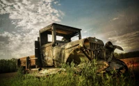 Voiture classique rustique au milieu de hautes herbes sous un ciel dramatique.