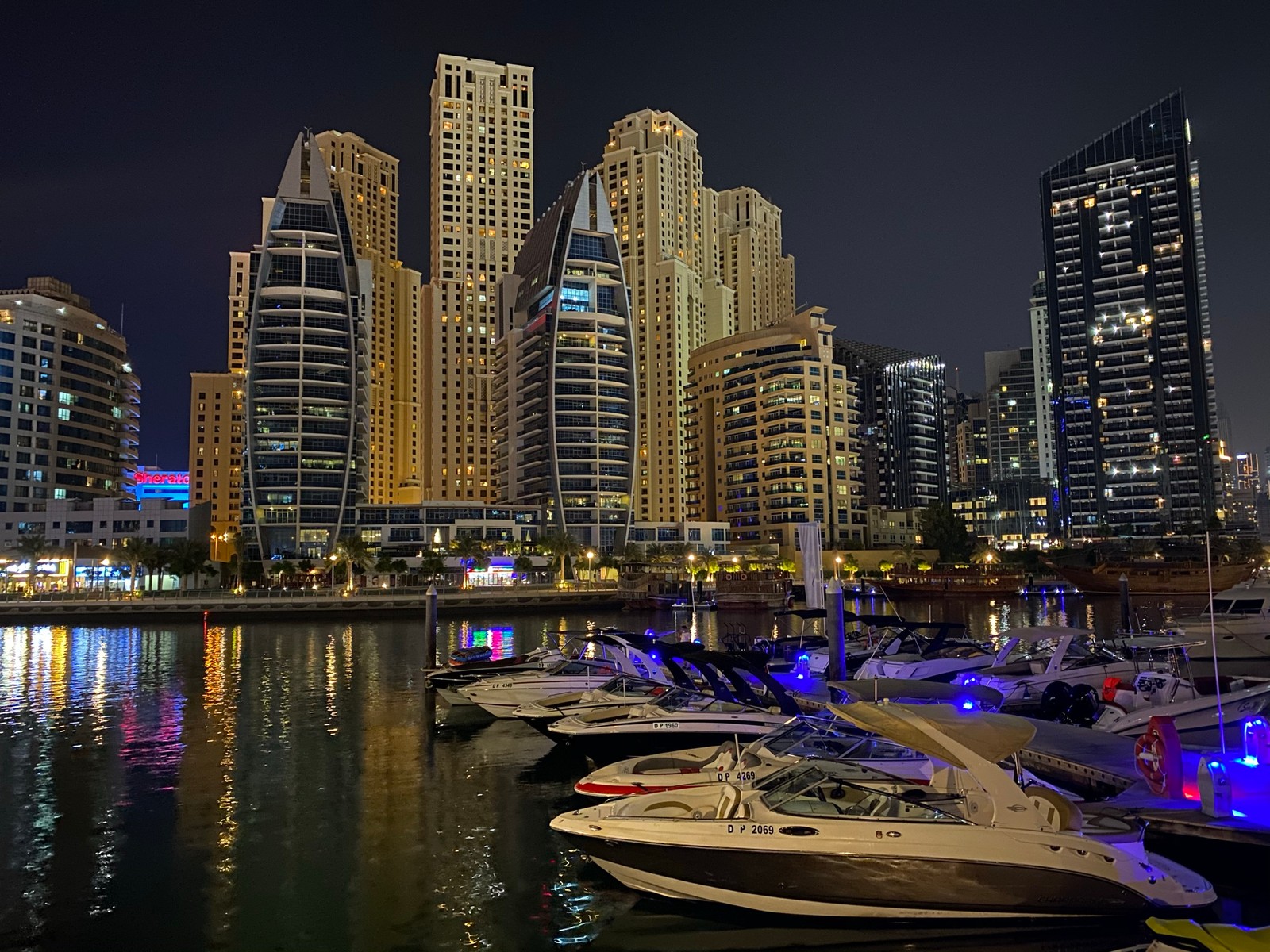 Las embarcaciones están atracadas en el agua frente a una ciudad por la noche (dubái, dubai, marina de dubái, paisaje urbano, rascacielos)