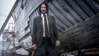 John Wick: Parabellum - Keanu Reeves in einem rauen Standoff neben einem verwitterten Schiff.