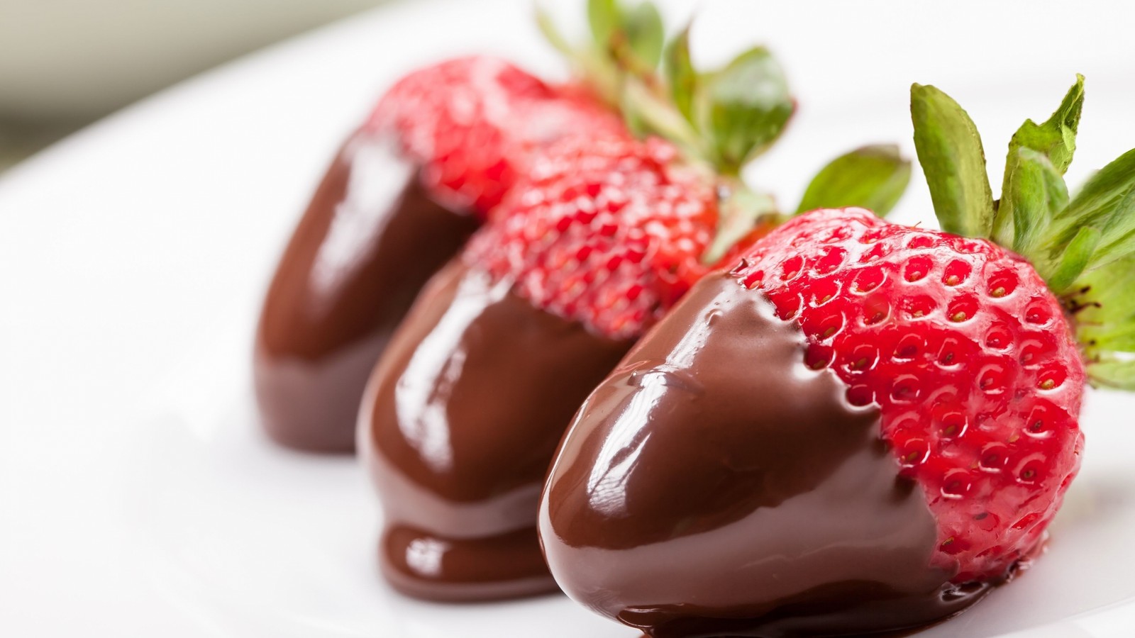 Schokoladenüberzogene erdbeeren auf einem weißen teller mit einem grünen blatt (schokolade, erdbeere, frucht, essen, süße)