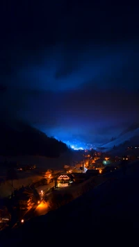 Illuminated Village in the Dusk with Mountains and Atmospheric Clouds