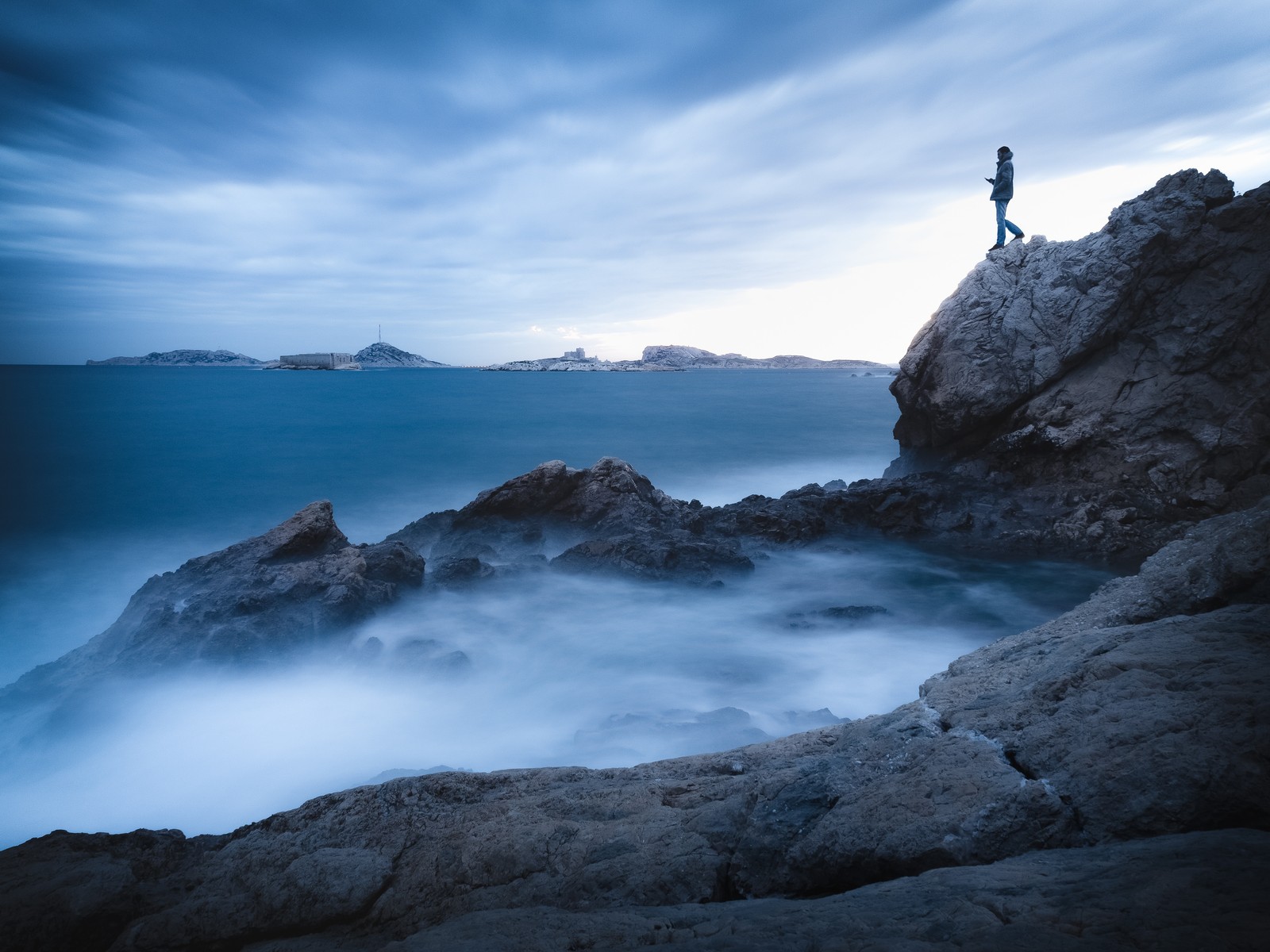 Un hombre de pie sobre una roca mirando el océano al atardecer (mar, océano, ola, agua, azul)