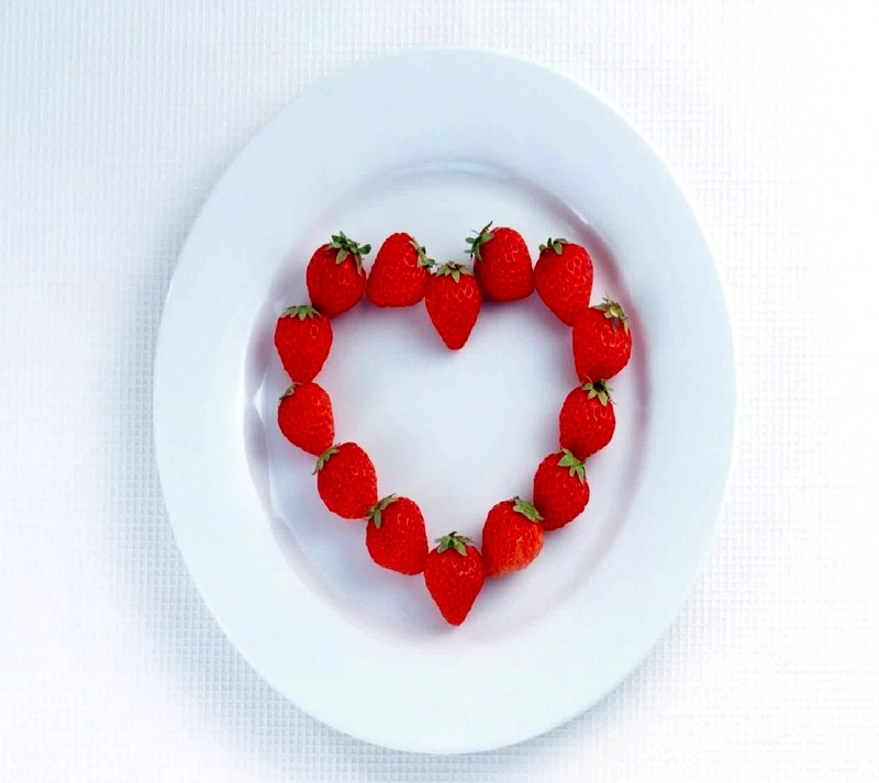 There is a heart shaped strawberry on a plate with a white background (love)