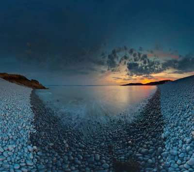 Pôr do sol costeiro sereno sobre a praia de seixos