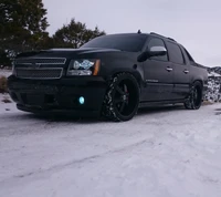 Caminhão Chevy Avalanche preto estacionado em uma estrada nevada, exibindo um design elegante e condições de inverno.