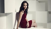 Elegant woman in a red dress, seated with a confident pose against a minimalist white backdrop.