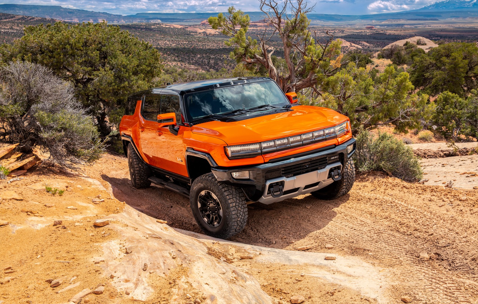 A orange truck driving down a dirt road in the mountains (gmc hummer ev, pickup truck, 2024, 5k, cars)