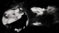 Batman silhouetté contre un ciel dramatique éclairé par la lune, entouré de nuages sombres et de pluie, évoquant une atmosphère d'humeur monochrome.