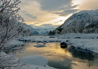 Tranquil Winter Landscape: Snow-Covered Mountains and Reflective Waters at Sunset