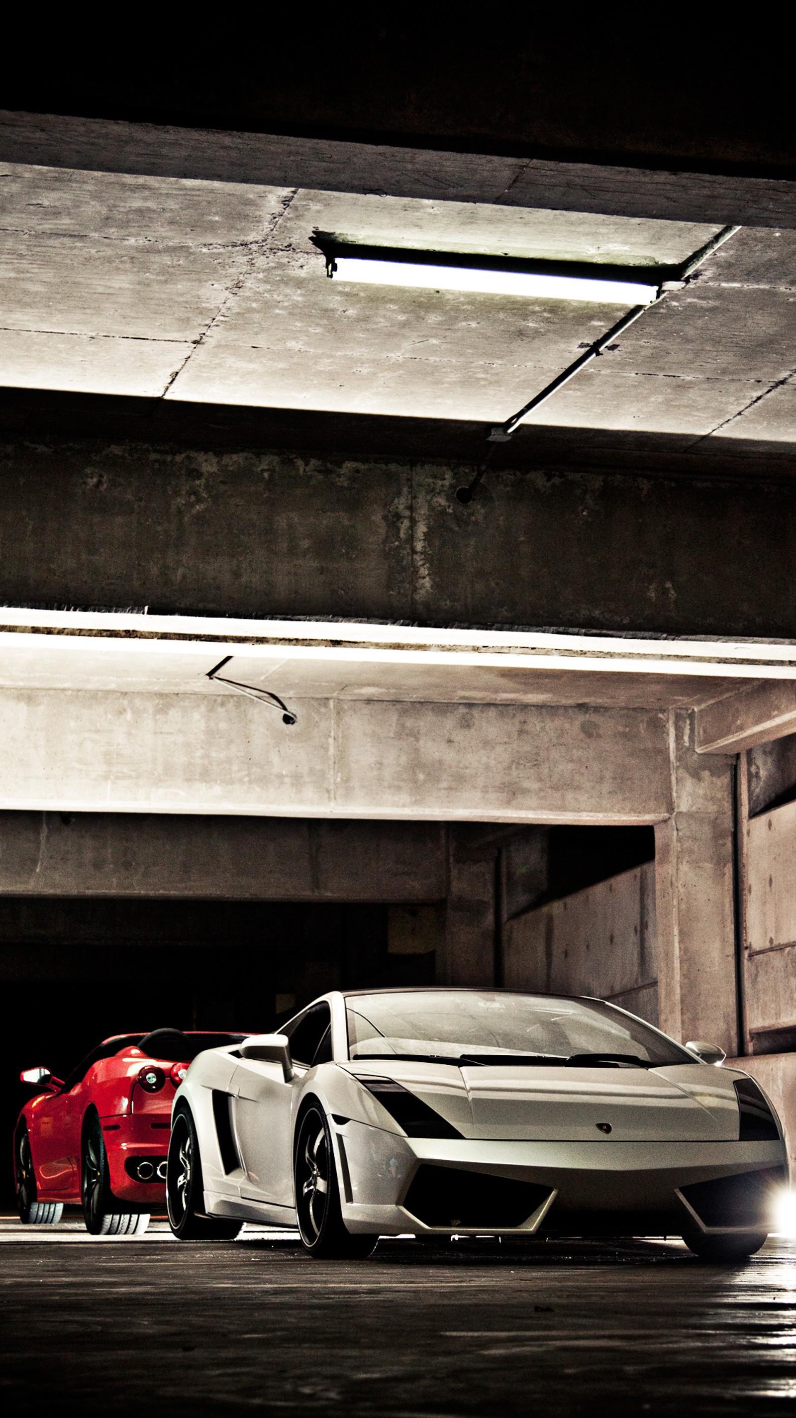 Two sports cars parked in a parking garage with a light on (cars, ferrari, lambo, park)