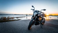 KTM 990 Super Duke estacionada junto al agua al atardecer, mostrando su diseño elegante contra un cielo vibrante.