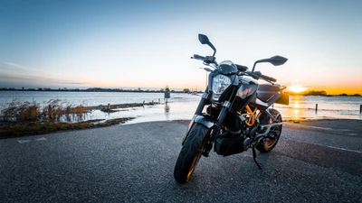 KTM 990 Super Duke parked by the water at sunset, showcasing its sleek design against a vibrant sky.