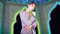 Doyoung from NCT U poses confidently in a stylish outfit, surrounded by vibrant neon lights in a uniquely designed setting.