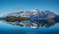 Snow-capped mountains rise majestically over a tranquil lake, their vivid reflection creating a serene tableau of nature's beauty.