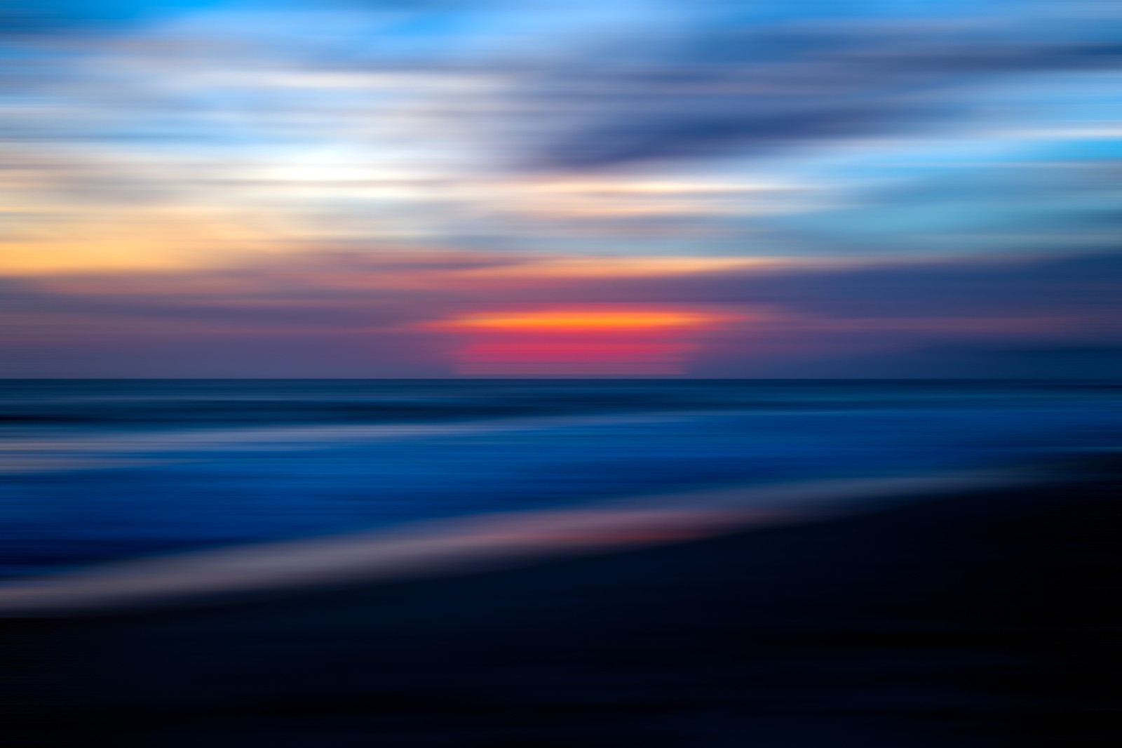 A blurry photo of a sunset over the ocean with a beach in the foreground (horizon, blue, sea, water, ocean)