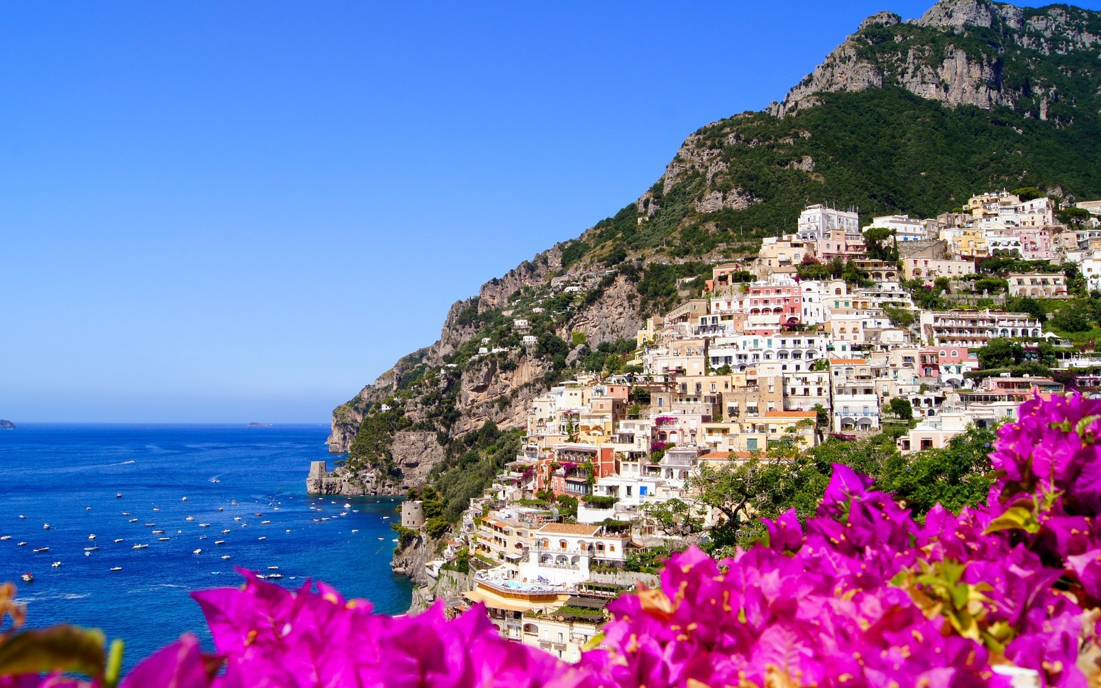 Vista de uma cidade na borda de um penhasco com flores à frente (sorrento, viagem, turismo, costa, mar)