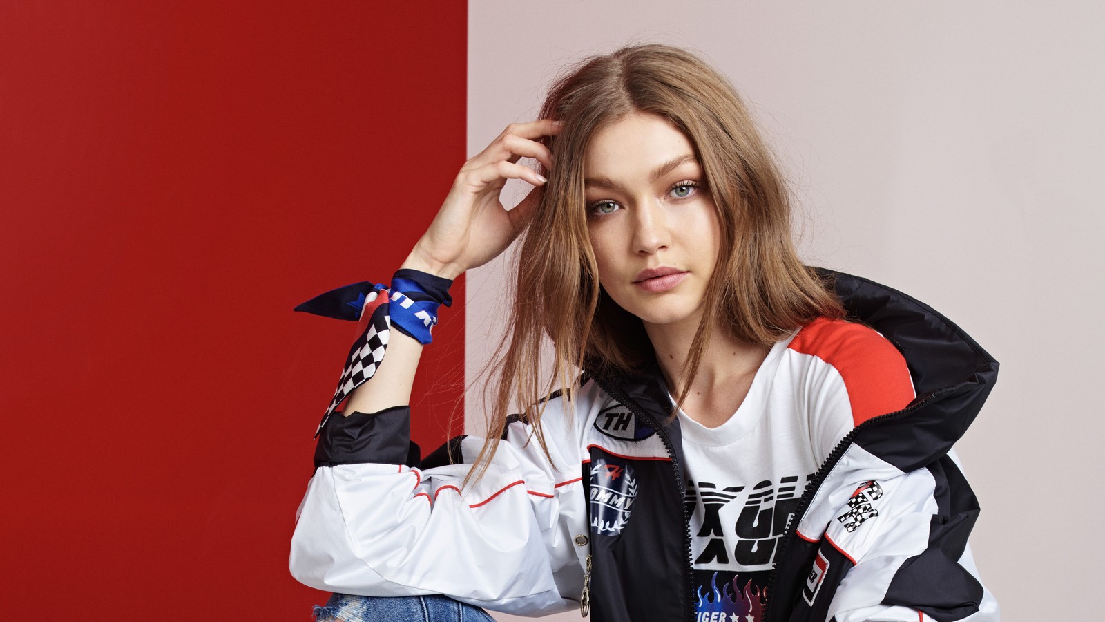 Femme arabe en veste blanche et jeans assise sur un mur rouge et blanc (gigi hadid, modèle, célébrité, célébrités, femmes)