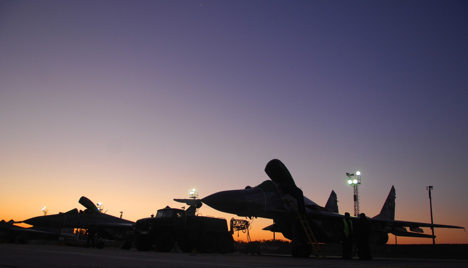 Aviões aráfidos sentados na pista ao pôr do sol em um campo (aeronave, avião de combate, força aérea, mikoyan mig 29, mikoyan gurevich mig 23)