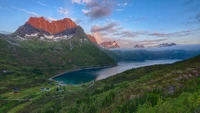 Deslumbrante paisagem de fiorde montanhoso ao amanhecer, apresentando um lago tranquilo cercado por terras altas acidentadas e uma majestosa cadeia de montanhas.