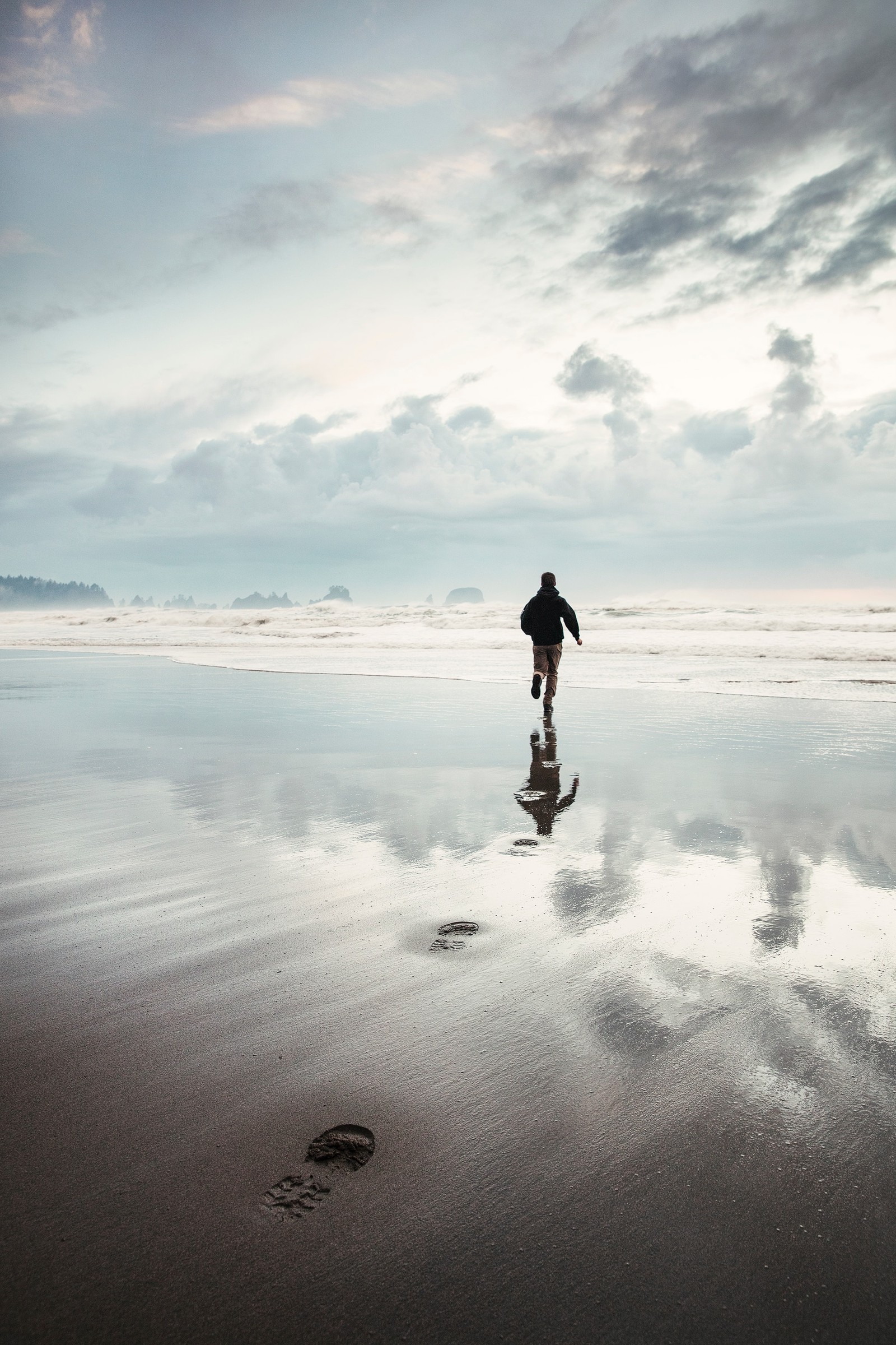 Há um homem caminhando na praia com uma prancha de surf (escala de cinzas, oceano, calmo, onda, horizonte)