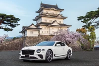 2021 Bentley Continental GT V8 Édition Équinoxe devant un château japonais traditionnel avec des cerisiers en fleurs.