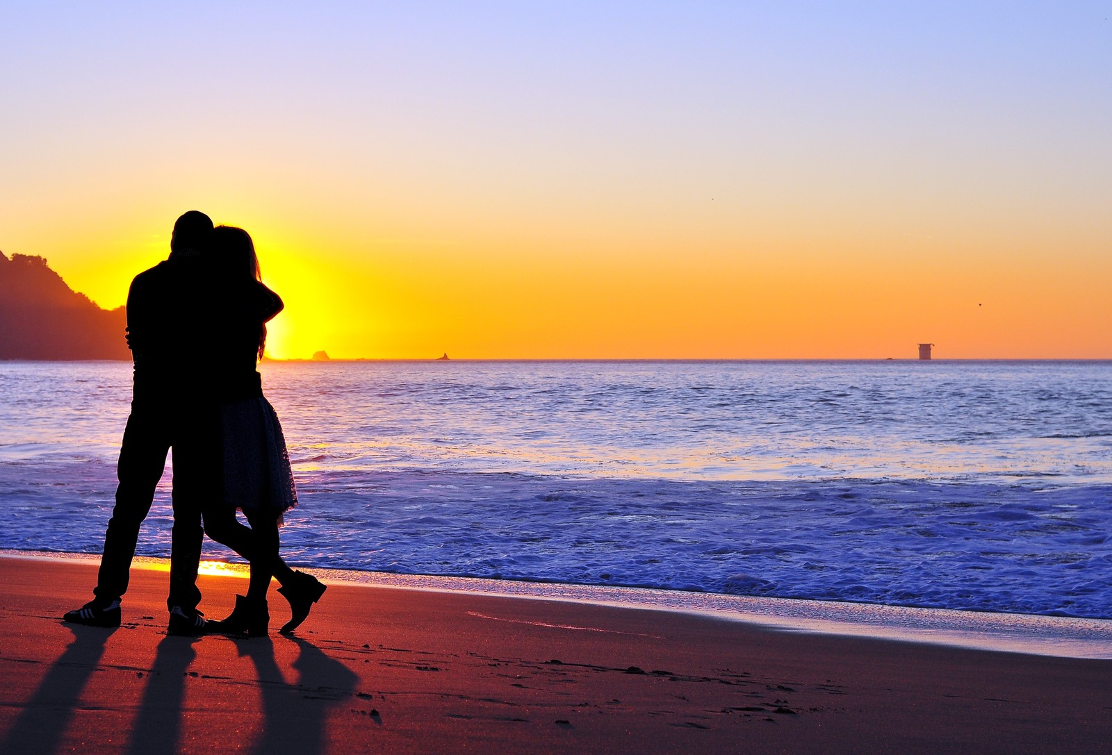 There are two people standing on the beach at sunset (couple, horizon, beach, sea, ocean)