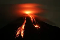 Erupting shield volcano at night, with flowing lava and volcanic ash against a dark sky.