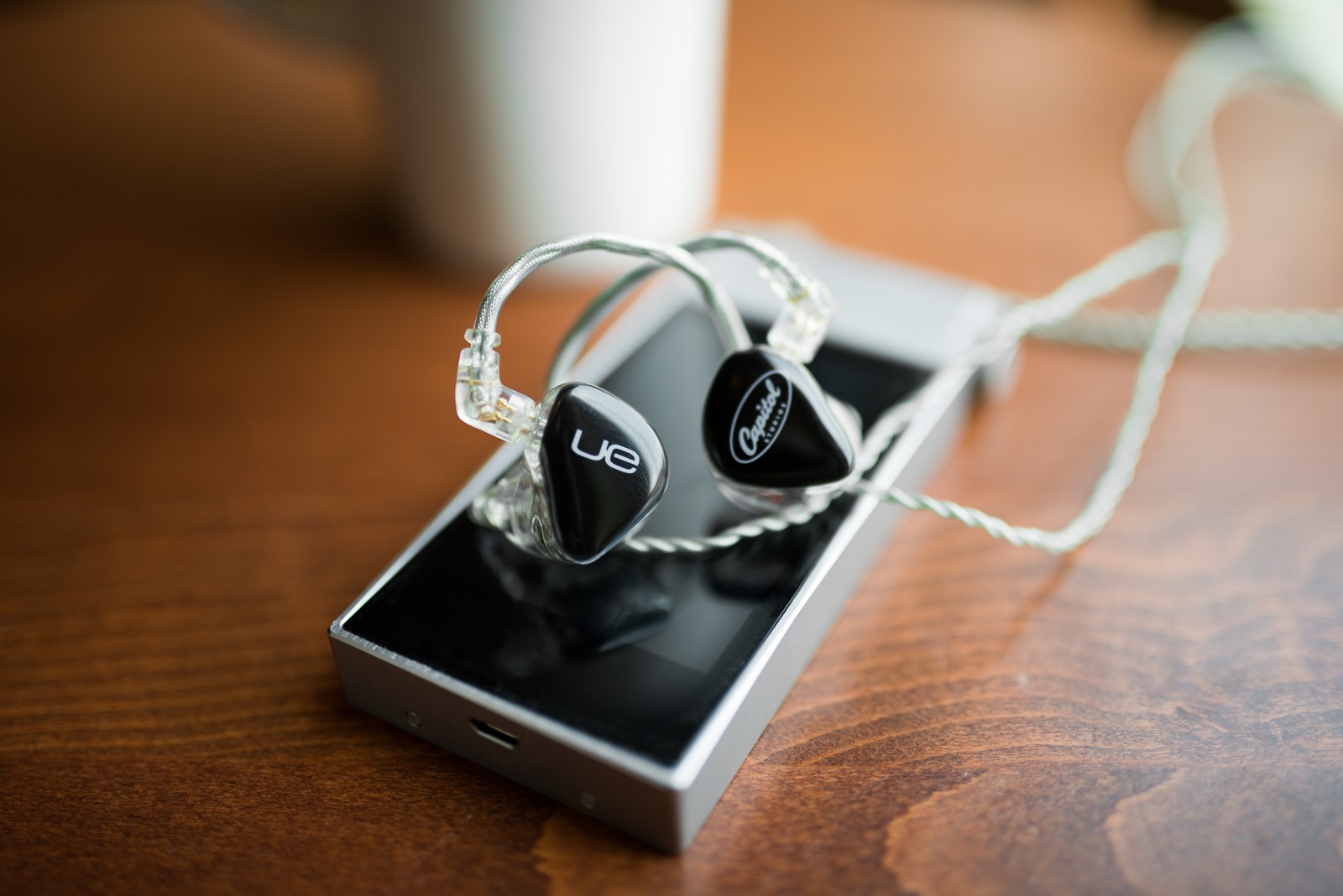 There is a cell phone with ear buds on it on a table (fashion accessory, gadget, jewellery, silver, audio equipment)