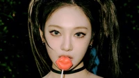 Ningning from Aespa with a playful expression, holding a lipstick-shaped lollipop against a dark, vibrant backdrop.