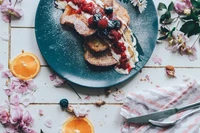 Torrada francesa fofa coberta com frutas vermelhas e creme, cercada por frutas frescas e flores delicadas.