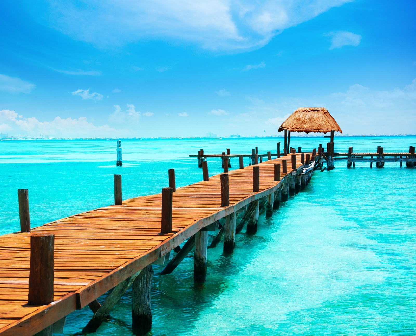 Un quai en bois arabe avec un parasol en paille au-dessus de l'eau (plage, bleu, génial, eau)