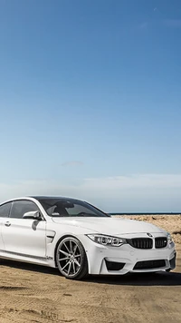 Eleganter weißer BMW M4 an einem sandigen Strand unter klarem blauen Himmel