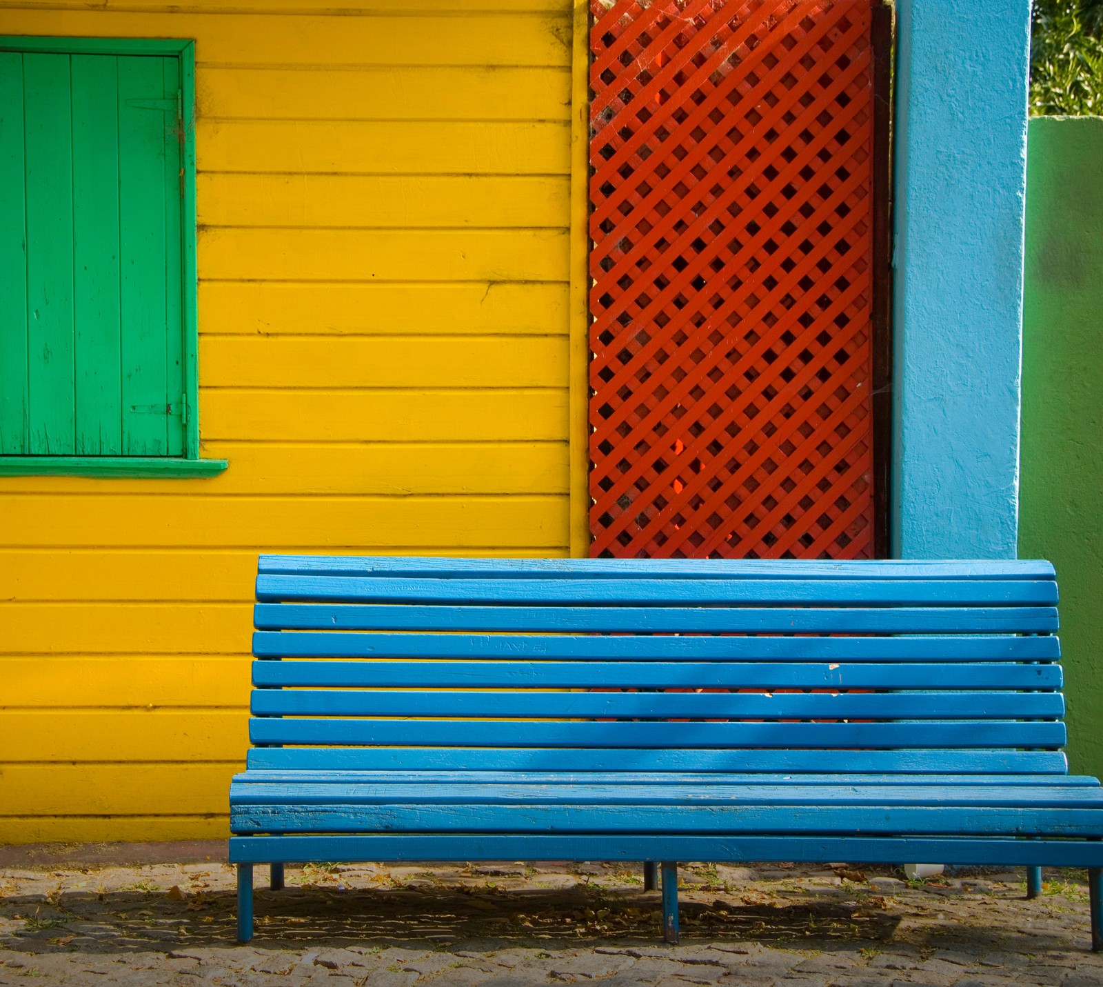 Brightly colored bench in front of a colorful building with a green door (bench, moto x, multicolor, wall)