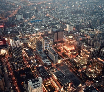 Vista aérea de uma paisagem urbana vibrante iluminada à noite, mostrando uma cidade movimentada com uma mistura de arquitetura moderna e edifícios densos.