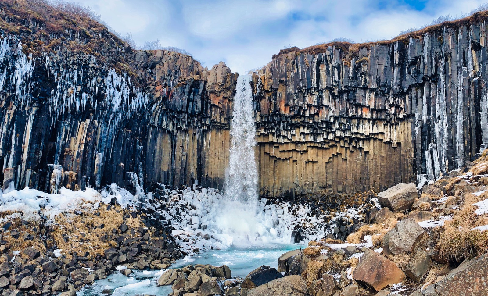 Uma cachoeira no meio de uma área rochosa com gelo nas pedras (cachoeira svartifoss, trilha svartifoss, svartifoss trail, islândia, parque nacional de vatnajökull)