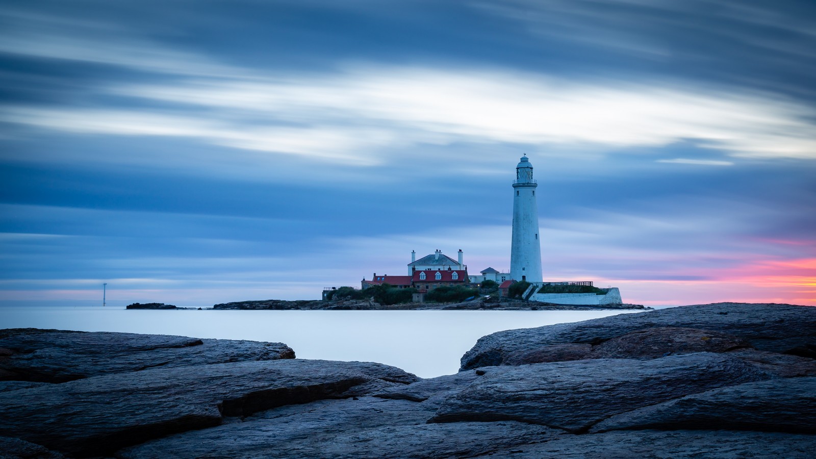 Uma vista de um farol em uma costa rochosa com um pôr do sol ao fundo (farol, nuvem, água, torre, edifício)