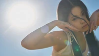 Nmixx Kyujin in a radiant Amor concept photo with a bright sun backdrop.