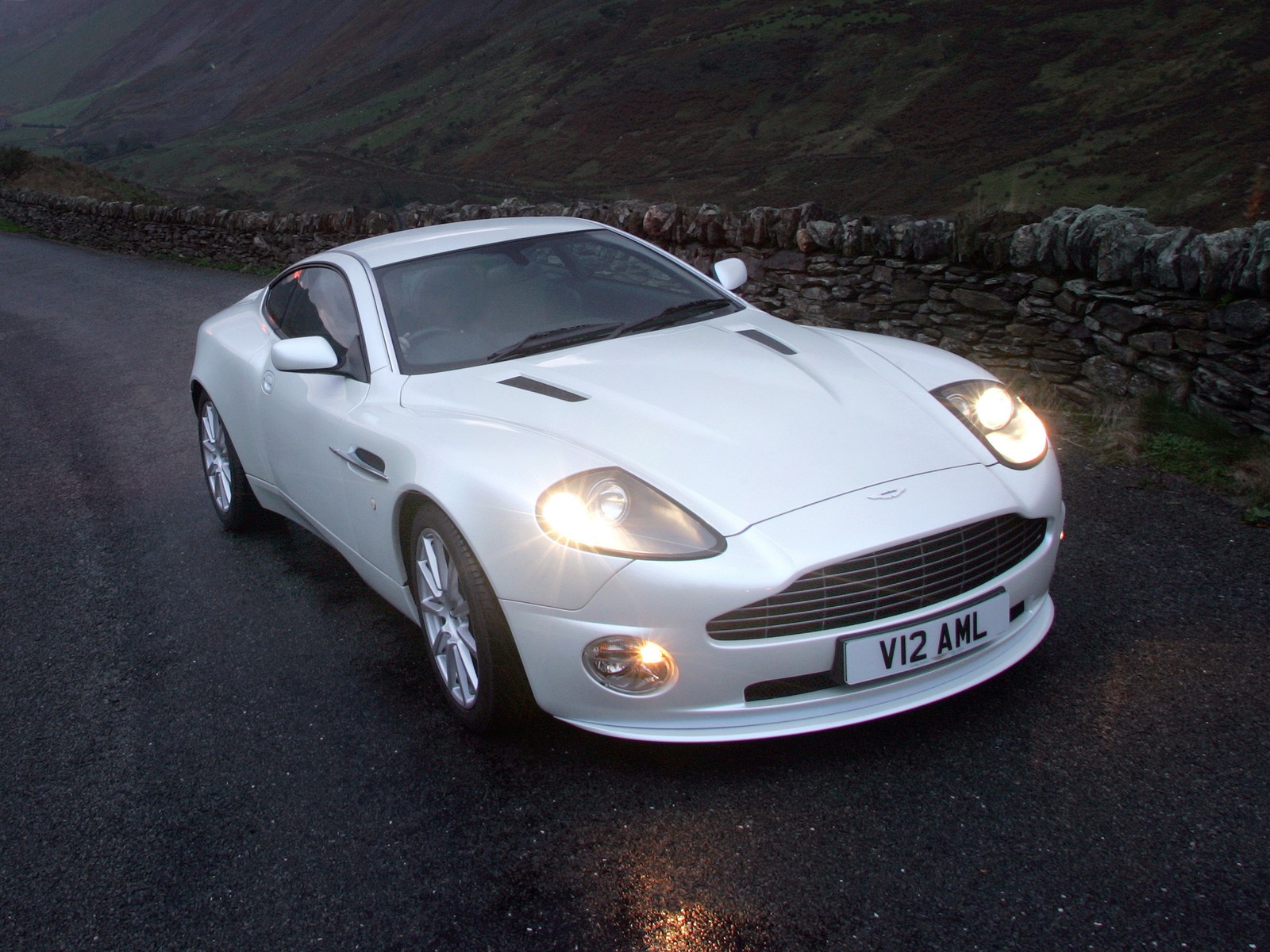 Une voiture de sport blanche roulant sur une route le soir (aston martin vanquish, aston martin, voiture de sport, voiture, aston martin db7)