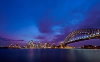 El Puente de la Bahía de Sídney y la Ópera contra un vibrante cielo púrpura al atardecer, mostrando un impresionante paisaje urbano iluminado por las luces de la ciudad.