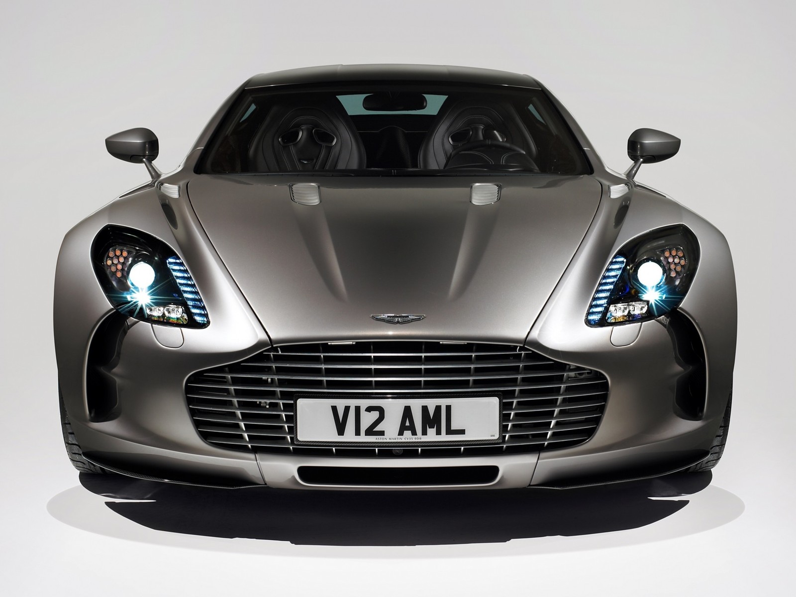 Um close de um carro prateado com uma placa (aston martin, supercarro, carro esportivo, aston martin vantage, aston martin one 77)