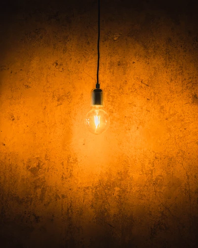 Warm Amber Glow of an Incandescent Light Bulb Against a Rustic Wall