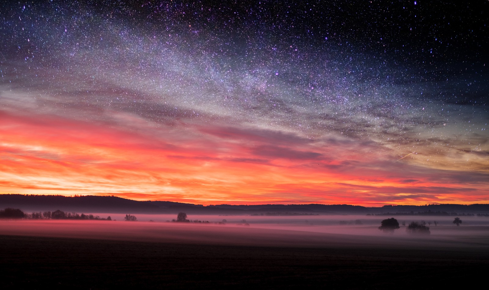 Vista de un campo con un cielo lleno de estrellas y algunos árboles (atardecer, resplandor, horizonte, naturaleza, amanecer)