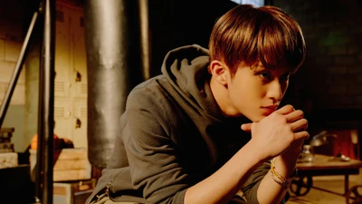 Mark Lee de NCT 127 dans une pose contemplative, affichant un look stylé avec un éclairage dramatique.